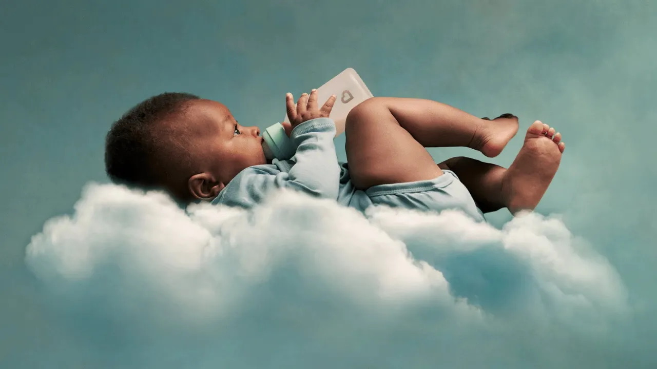 A baby resting on a soft cloud while a bottle is offered