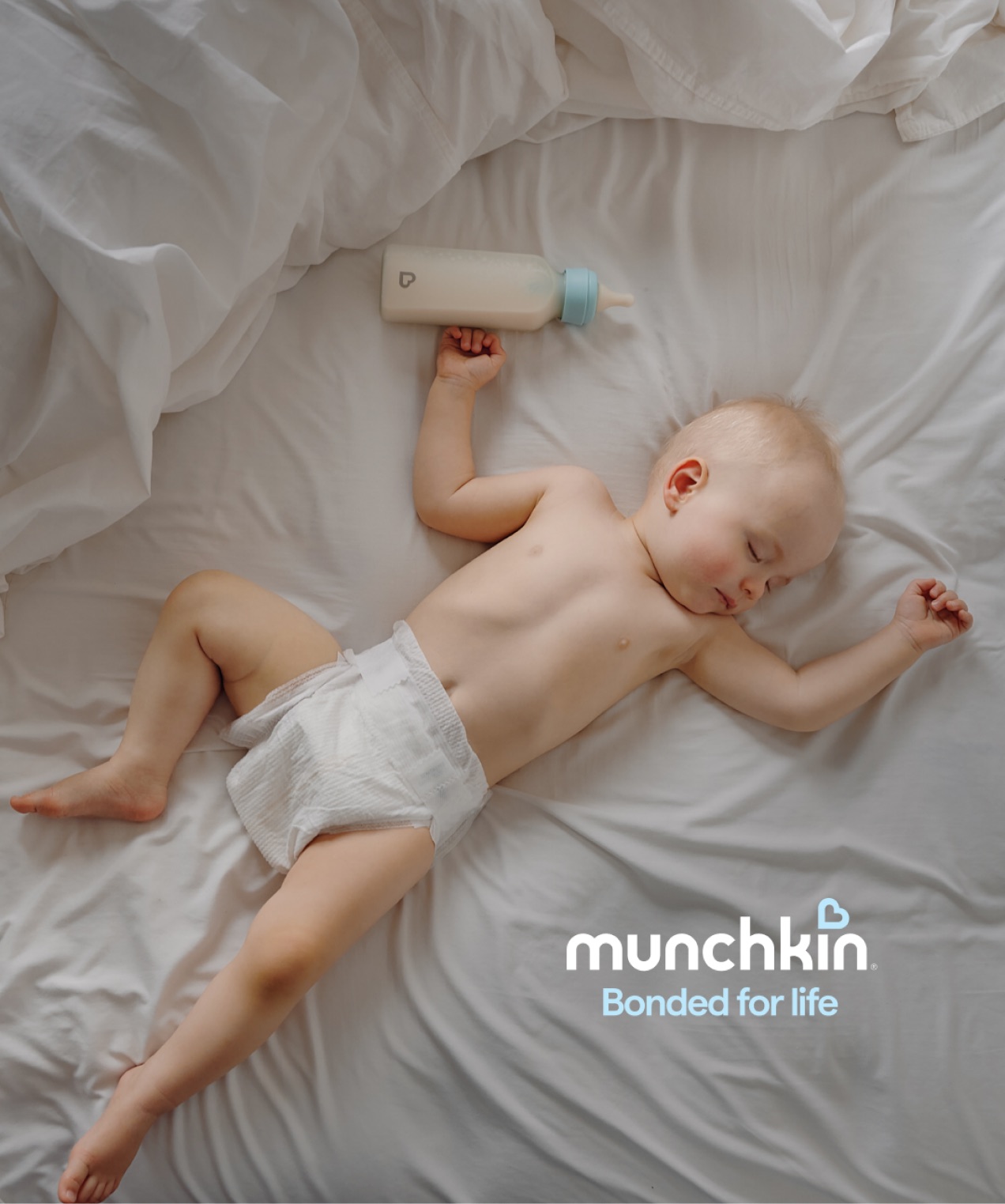 A baby lying on a bed beside a Bond bottle