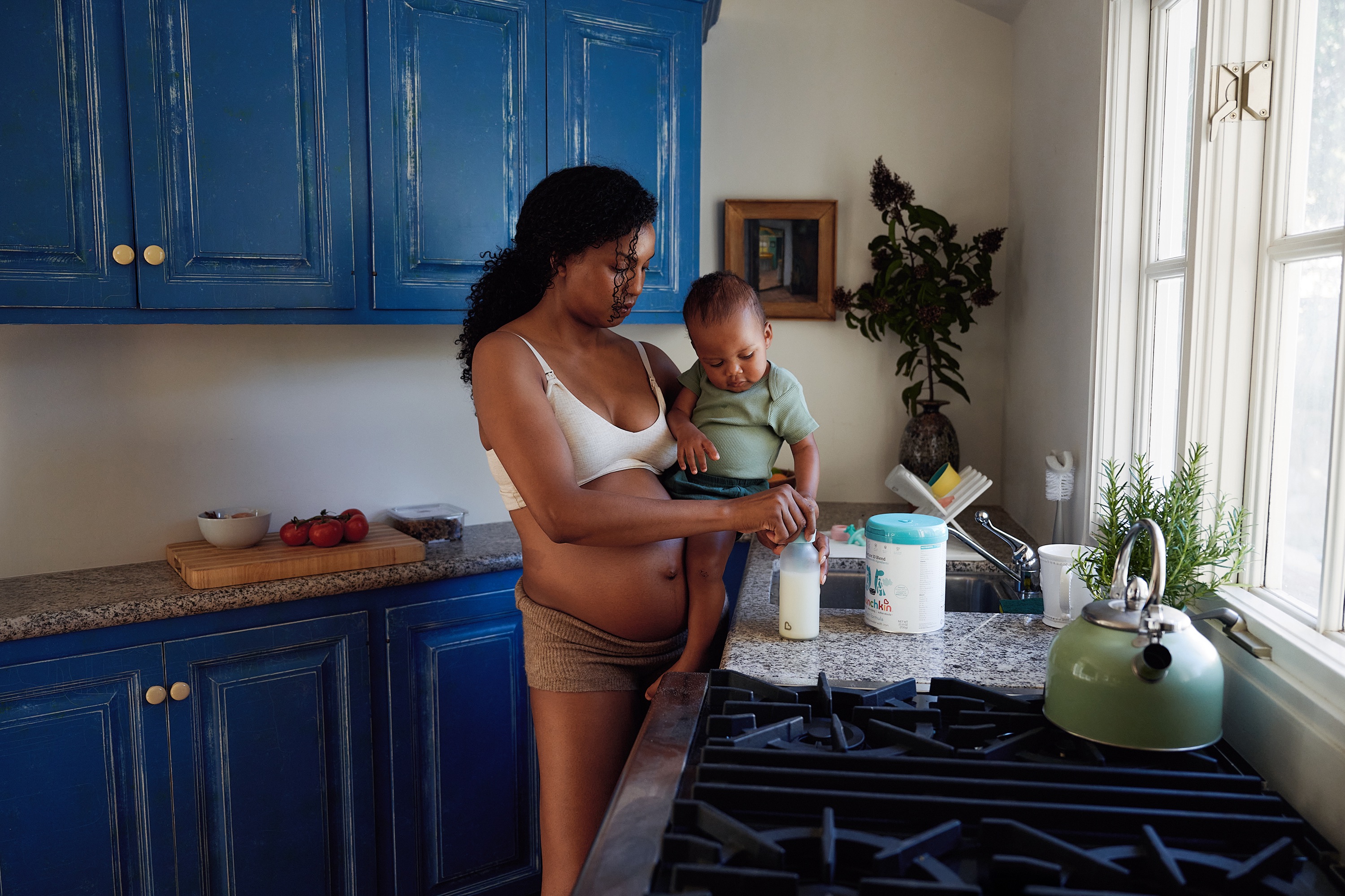 A mother holding her toddler while preparing a bottle in a kitchen