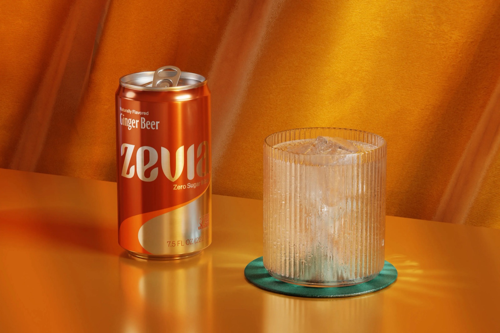 A Zevia Ginger Beer can beside a ribbed glass of ice on an amber surface