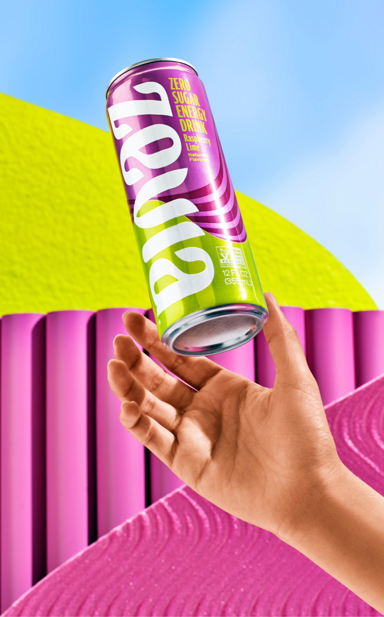 A hand holding a Zevia Energy can against a bright sky and pink shapes