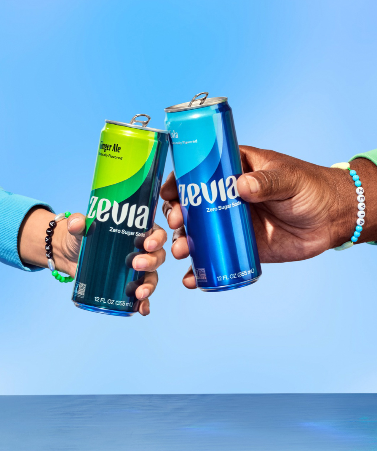 Two hands clinking Zevia cans above a blue mirrored block
